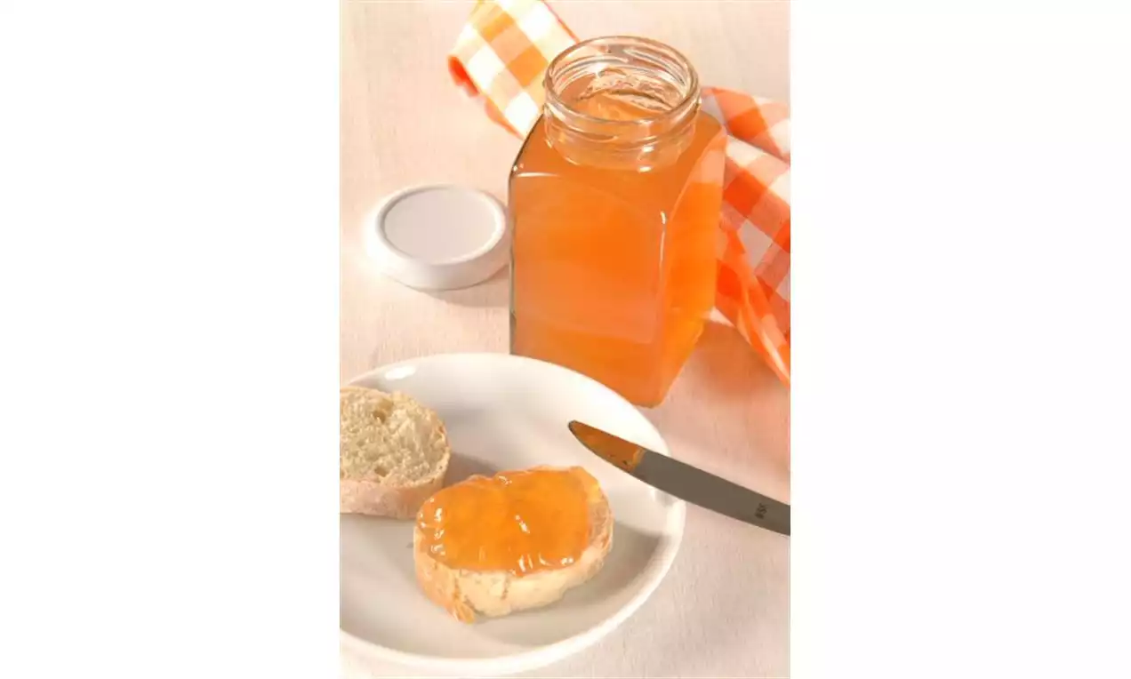 Mispelgelee in einem eckigen Glas mit weißem Deckel, daneben ein angerichtetes Brötchen auf weißem Teller, orange-weiß kariertes Tuch im Hintergrund