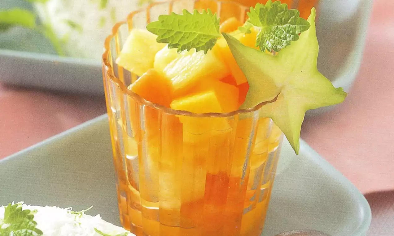 Morceaux de fruits jaune et orange dans un verre texturé, garnis de feuilles de menthe et d'une étoile de carambole sur un plateau bleu