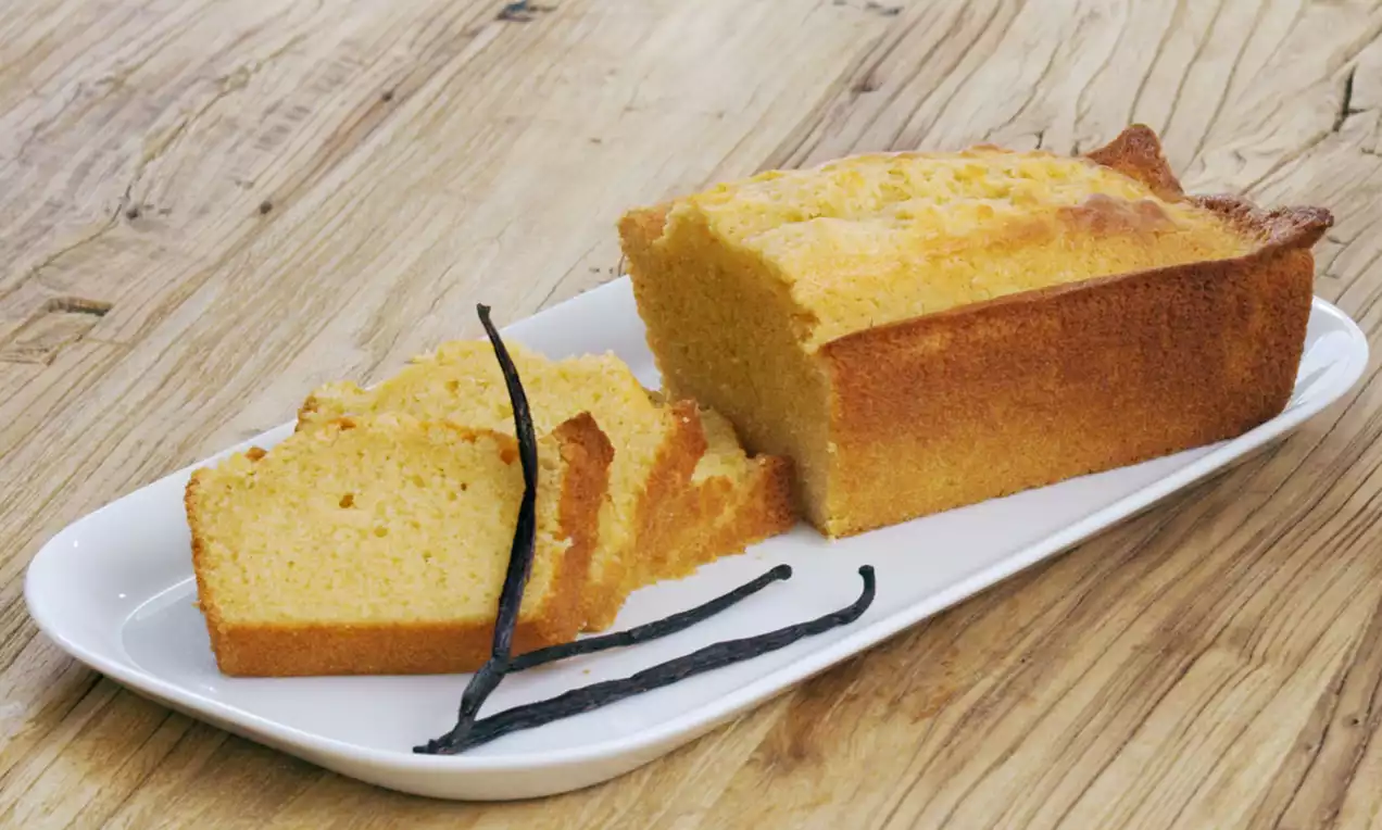 Cake doré à la vanille moelleux avec une croûte légèrement brunie, découpé en tranches sur une assiette blanche avec des gousses de vanille