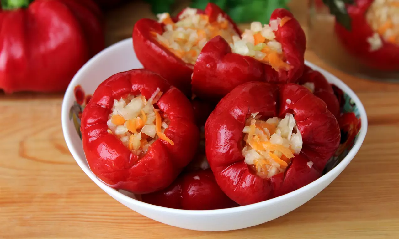 Яркочервени камби с гладка кожа, пълнени с ситно нарязано зеле и моркови, поднесени в бяла купа върху дървена повърхност