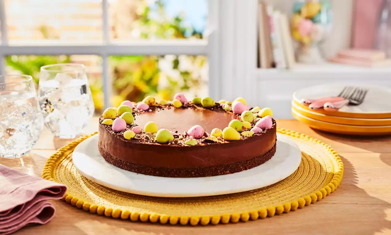 Smooth dark chocolate cheesecake with an even surface, topped with pastel mini eggs and crumbs, resting on a white plate