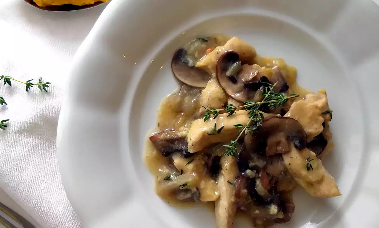 Světlé kuřecí kousky zalité krémovou hořčicovou omáčkou, hnědé plátky žampionů a snítky čerstvého tymiánu na bílém porcelánovém talíři