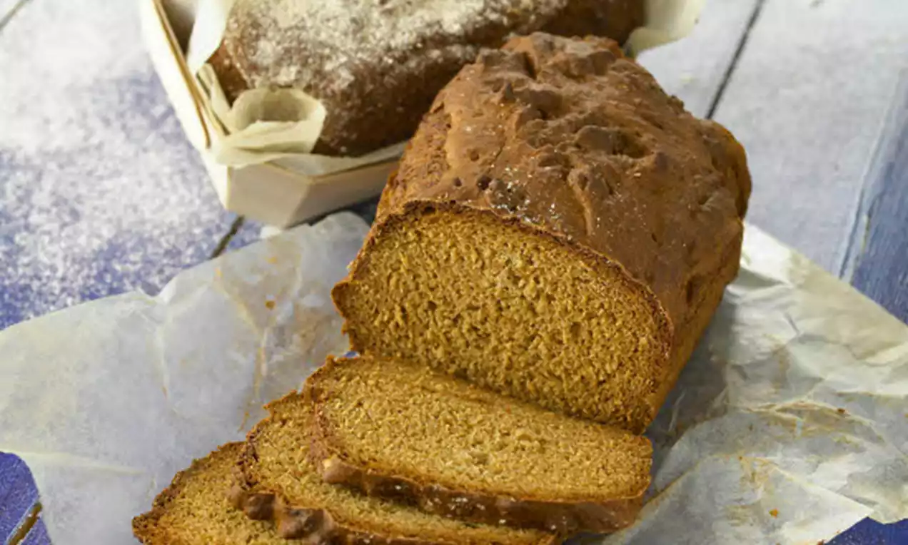 Filmjölkslimpa med mørkebrunt brød, skiver lagt frem foran et helt brød drysset med mel på bakepapir, på et blåmalt trebord