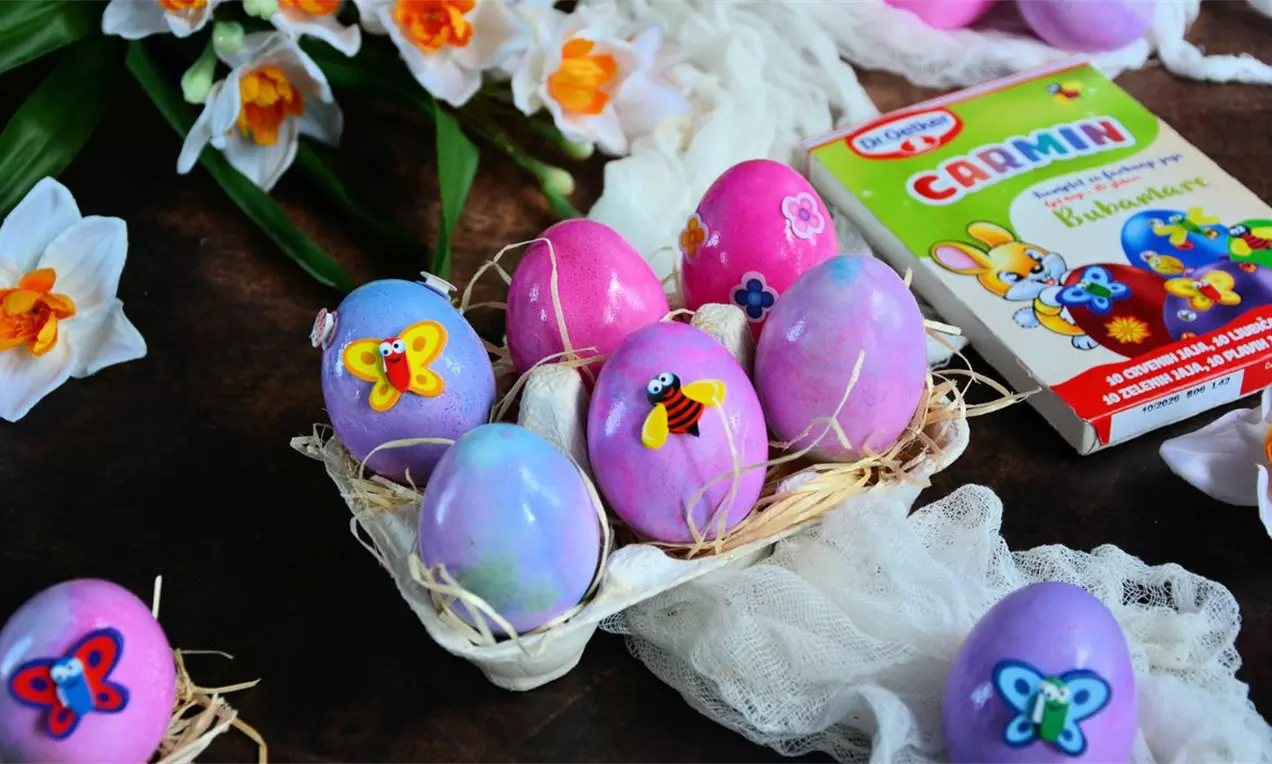 Šarena vaskršnja jaja pastelnih tonova položena na slamastu podlogu u kartonskoj kutiji, ukrašena nalepnicama leptira