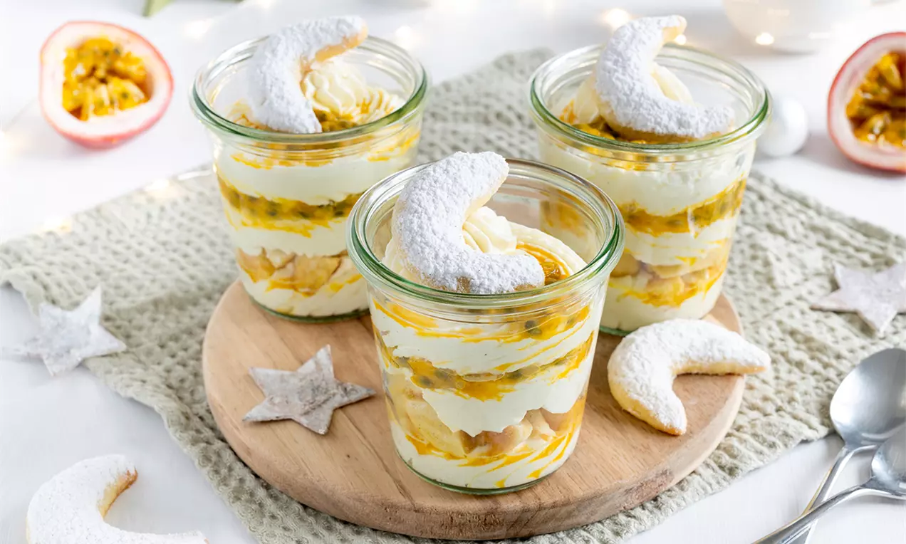 Vanillekipferl-Tiramisu mit gelber Passionsfruchtsoße in Gläsern geschichtet, dekoriert mit Puderzucker-Kipferln auf Holzplatte