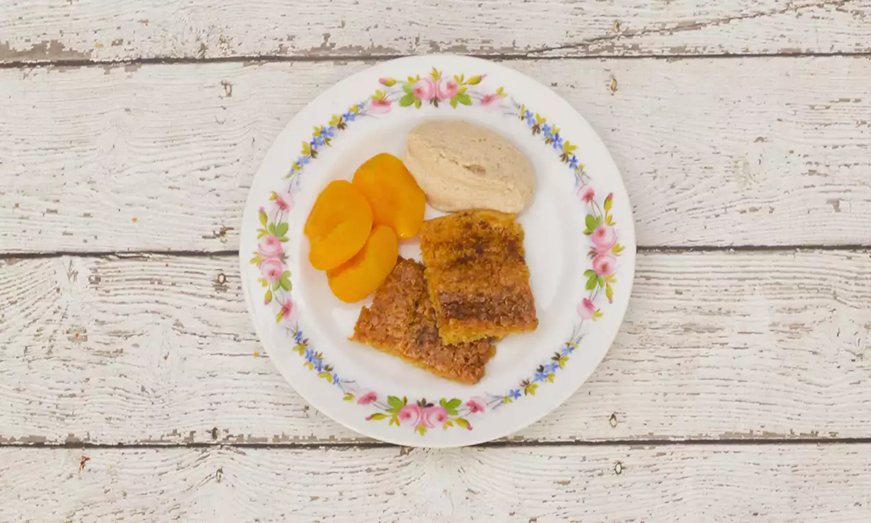 Carrés dorés à la texture moelleuse avec des tranches orange vif et une quenelle crème beige sur une assiette fleurie blanche