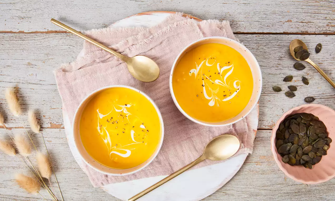 Hokkaido-Suppe in weißer Schale, samtig orange, garniert mit gerösteten Kürbiskernen, Petersilie und Crème fraîche