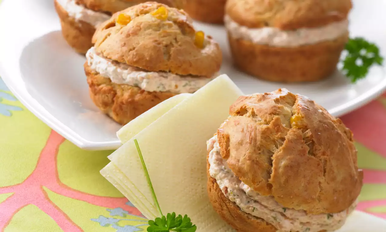 Goldbraune Schinkenmousse-Cupcakes mit lockerer Füllung, serviert auf weißem Teller und bunter Tischdecke, dekoriert mit Petersilie und Serviette