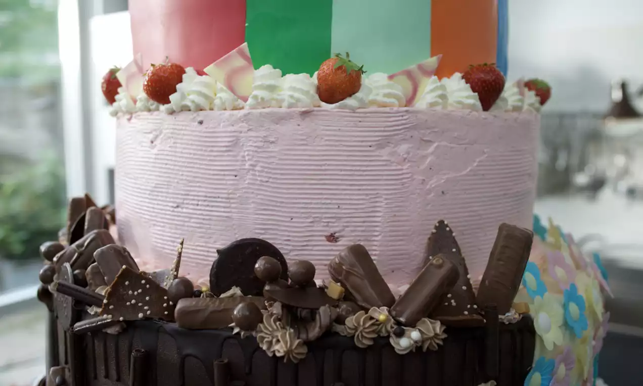 Meerkleurige taart met roze kwarklaag, decoratieve aardbeien, slagroomtoefjes, chocolade-elementen en een glanzende bovenlaag