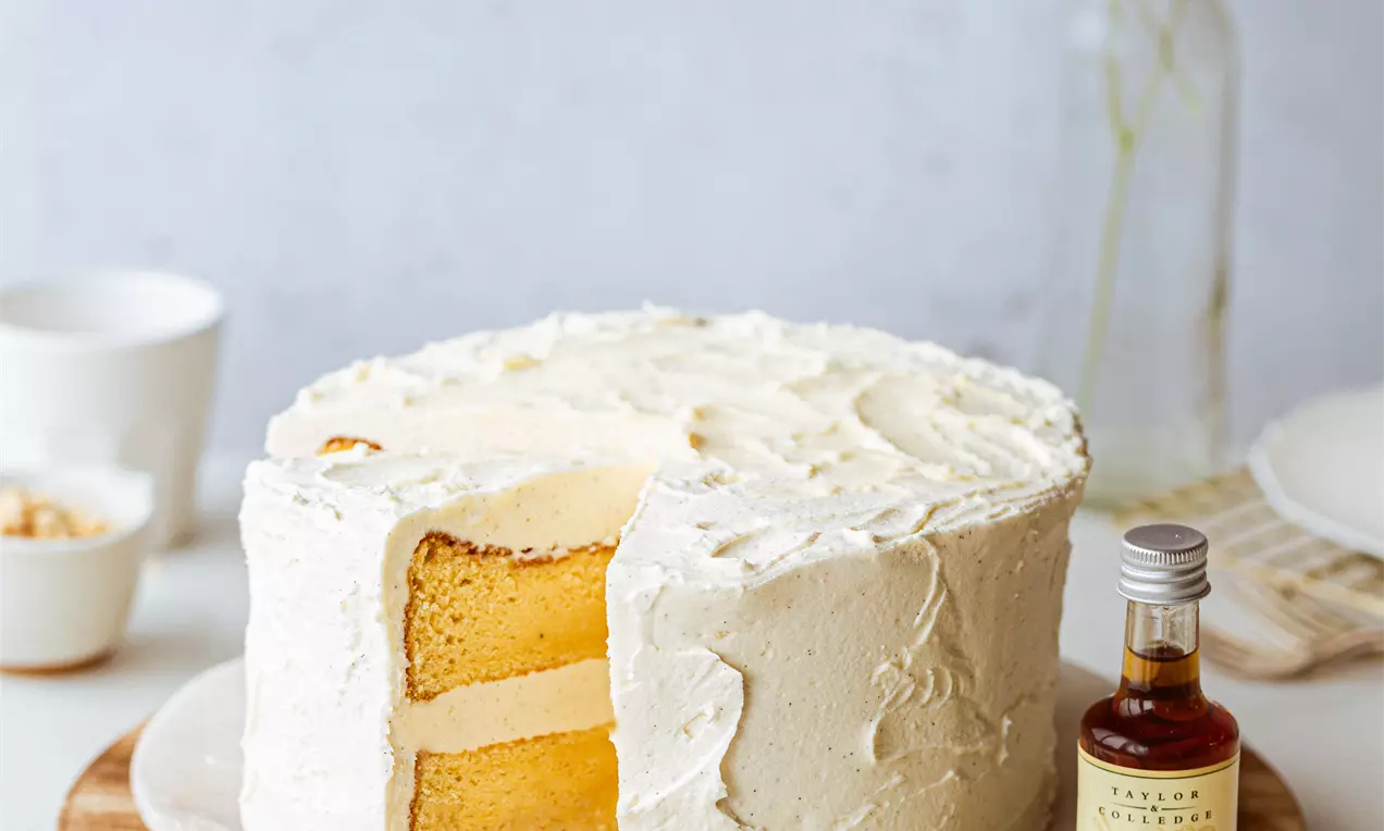 Pyöreä vaniljakakku kermaisen vaalealla kuorrutteella, siistit leikatut kerrokset vaaleankeltaista kakkua valkoisella tarjoiluvadilla