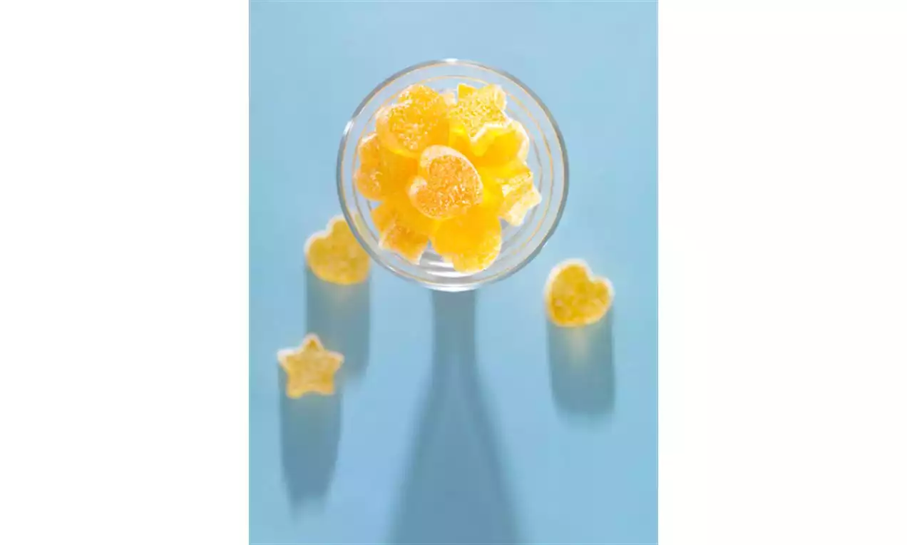 Gule, sukkerovertrukne sitronformede godteribiter i en glasskål med stjerner og hjerter plassert rundt på en lys blå bakgrunn