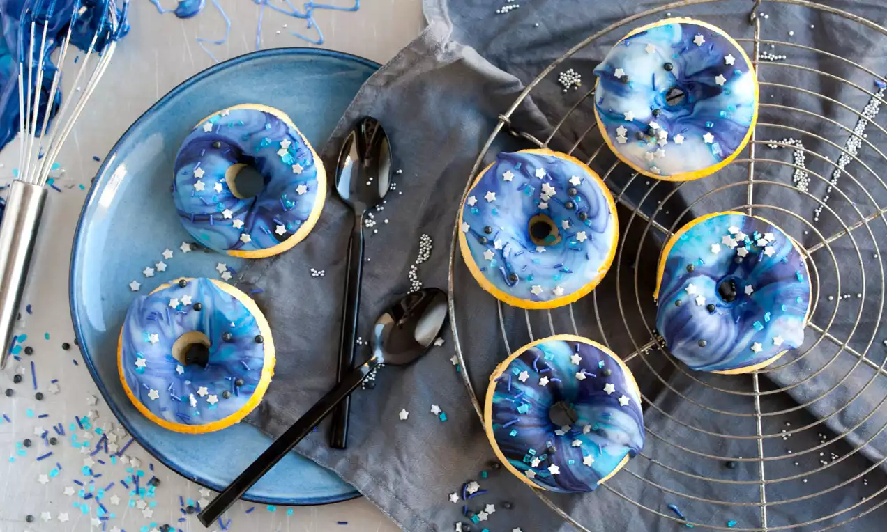 Donuts mit glänzender blauer Glasur und weißem Sternkonfetti, kreisförmig auf einem Metallgitter und blauem Teller arrangiert