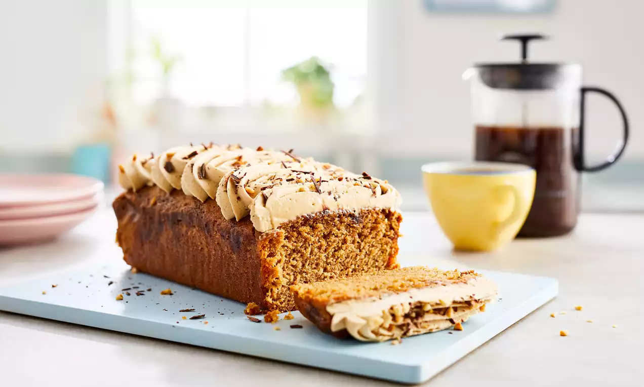 Rektangulär kaffekaka med ljusbrun glasyr och chokladströssel, skuren skiva bredvid, placerad på ljusblå skärbräda