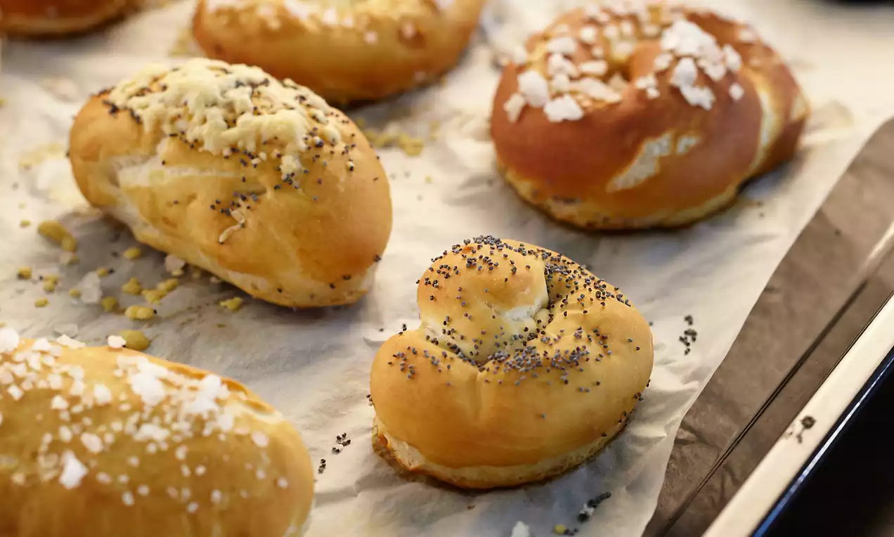 Goldbraunes Laugengebäck mit Salz- und Mohnstreuseln auf Backpapier, unterschiedlich geformt und locker angeordnet