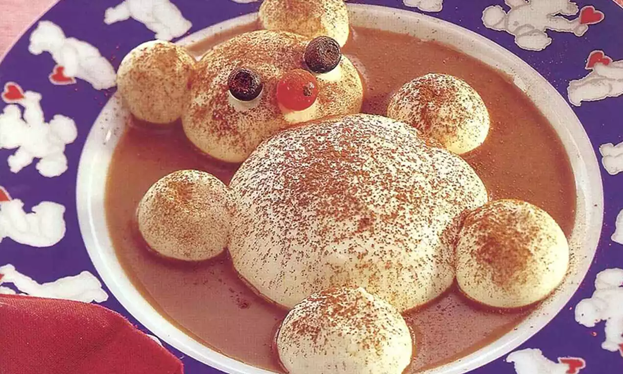 Ours en mascarpone poudré de cacao avec des yeux myrtilles et un nez cerise, flottant dans une assiette bleu ornée de motifs blancs