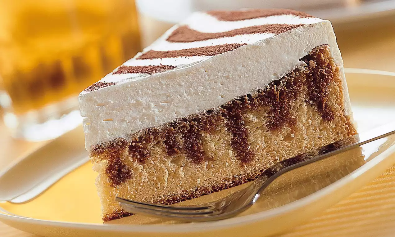 Part de gâteau moelleux marbré au whisky, surmontée d'une crème épaisse blanche et de motifs poudrés bruns, sur une assiette beige