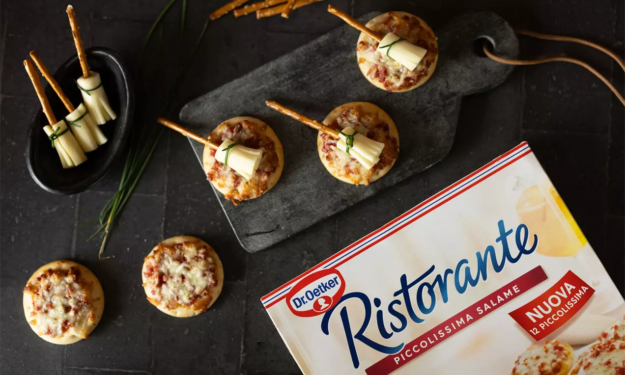 Mini Halloween-pizza's met gesmolten kaas en rode salami op een donkere plank, omringd door zoute snacks en taaie kaasrolletjes