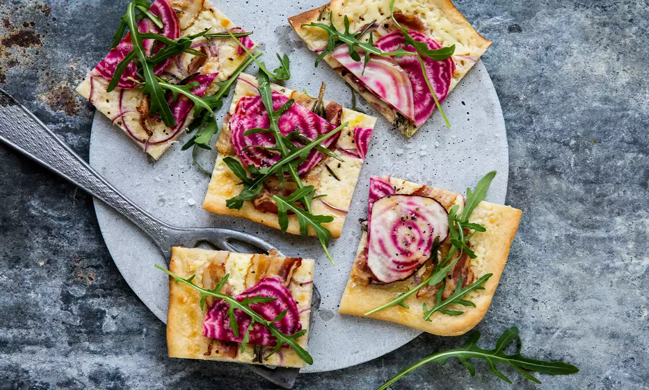 Carrés de tarte dorée garnis de fines tranches de betterave Chioggia rose et blanche, roquette verte et filet de vinaigrette