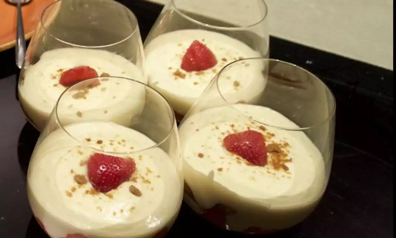Tiramisu en verrines aux couches crémeuses ivoire garnies de fraises rouge vif et parsemées de miettes dorées sur un plateau noir