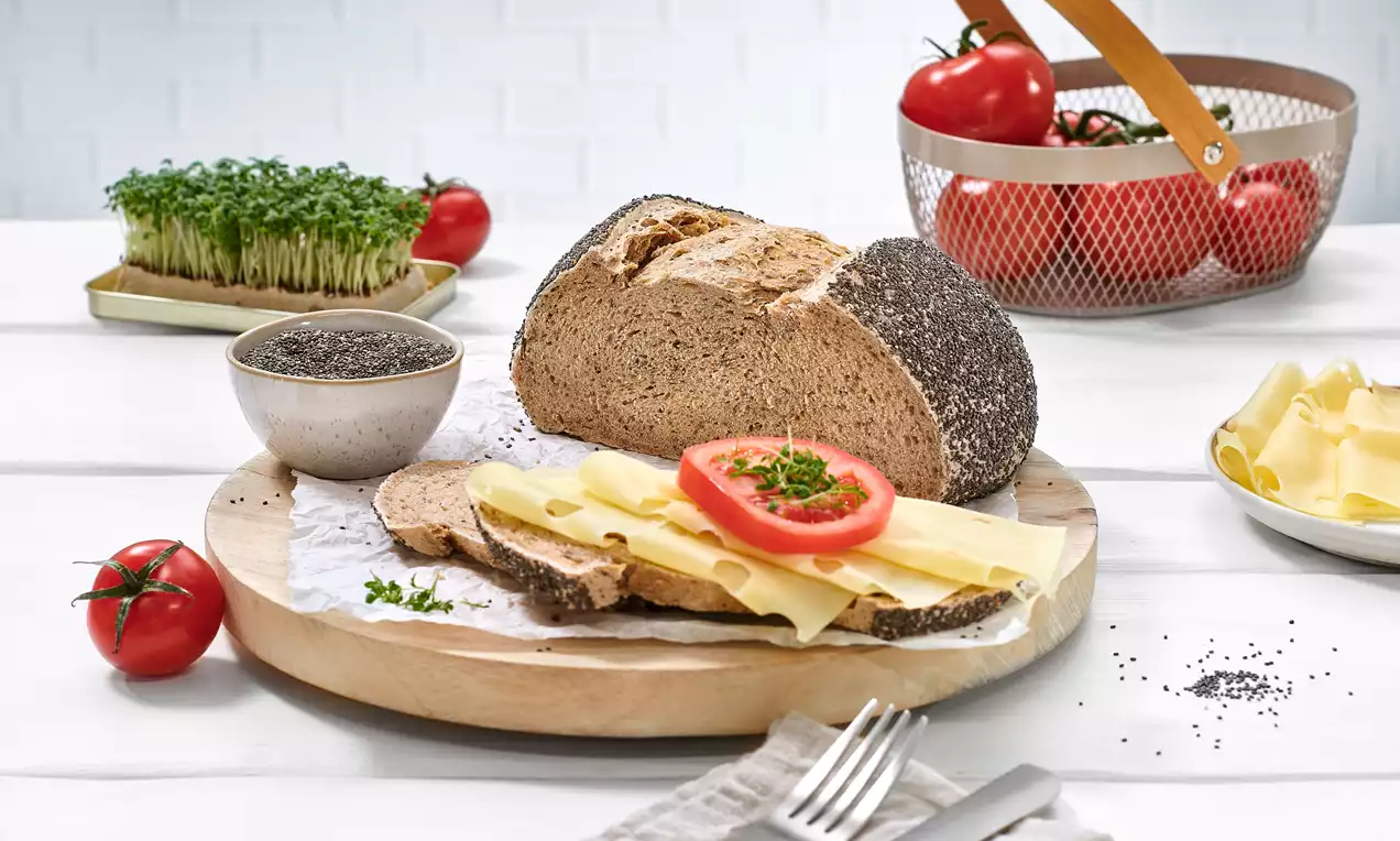 Chiabrot mit goldbrauner Kruste und schwarzem Chiarand, angerichtet auf einem Holzbrett mit Käsescheiben, Tomate, Kresse und Chiasamen