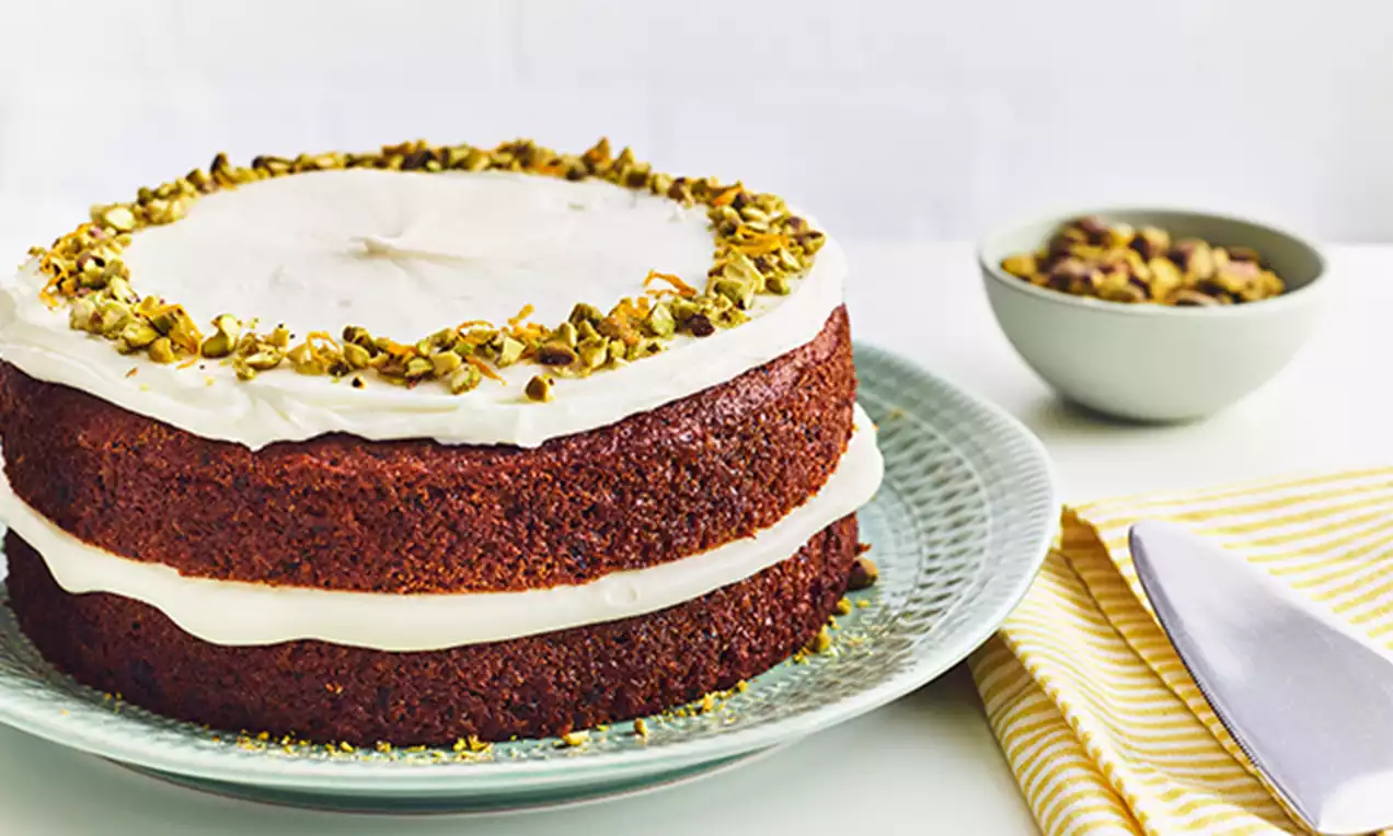 Vegansk gulrotkake med to lag saftig, gyllenbrun kake fylt med hvit krem, toppet med hakkede pistasjnøtter på et grønt fat