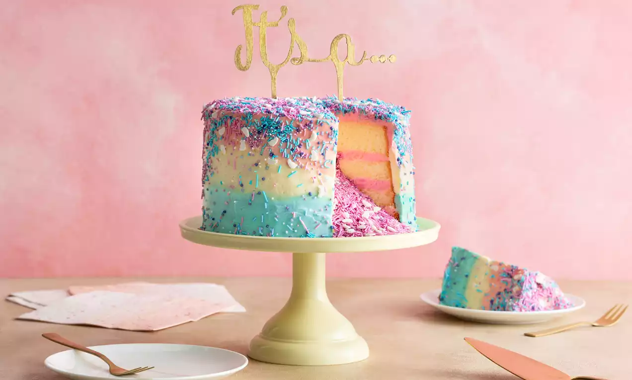 Ronde gender reveal taart met blauwe en roze laagjes, bedekt met gekleurde glazuur en sprinkles op een pastel taartplateau