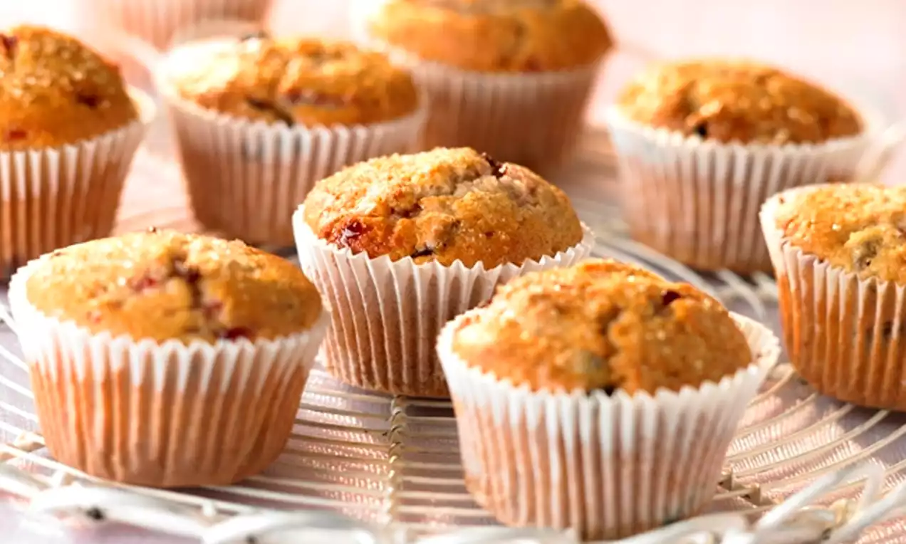 Golden-brown muffins with slightly domed tops studded with red Morello cherry pieces in white paper cups on a wire rack