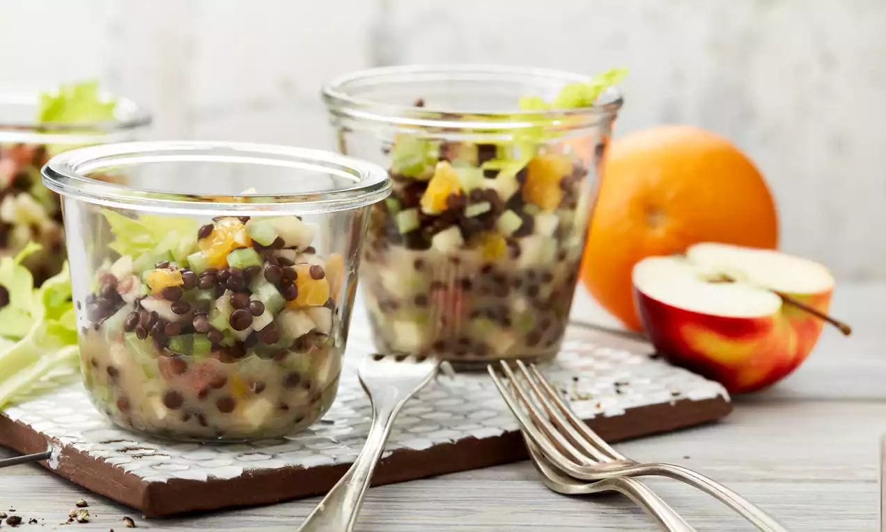 Fruchtiger Linsensalat aus schwarzen und roten Linsen, Apfelstücken und Orangenspalten, hübsch arrangiert in klaren Gläsern mit Gabeln daneben