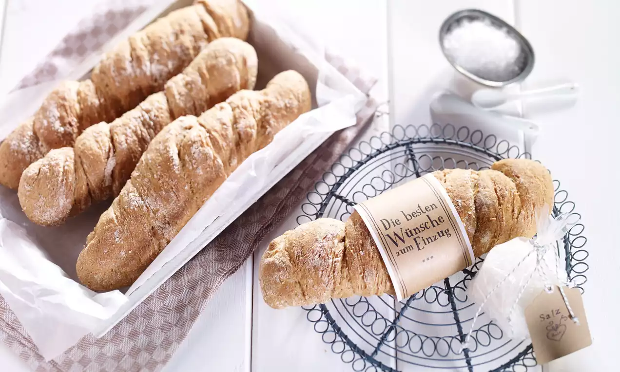 Vaaleanruskeat, jauhoiset spelttikierresämpylät, karkeapintaisia ja pitkänomaisia, aseteltuina vaaleassa korissa ja metalliritilällä