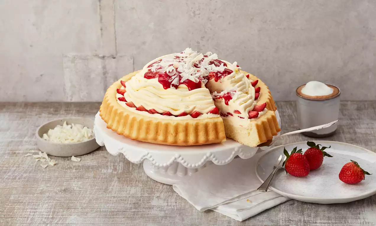 Spaghetti-Eis-Kuchen mit weißer Sahnecreme, roten Erdbeersoßen-Tupfen, weißen Schokoraspeln auf gewelltem Boden auf weißer Tortenplatte