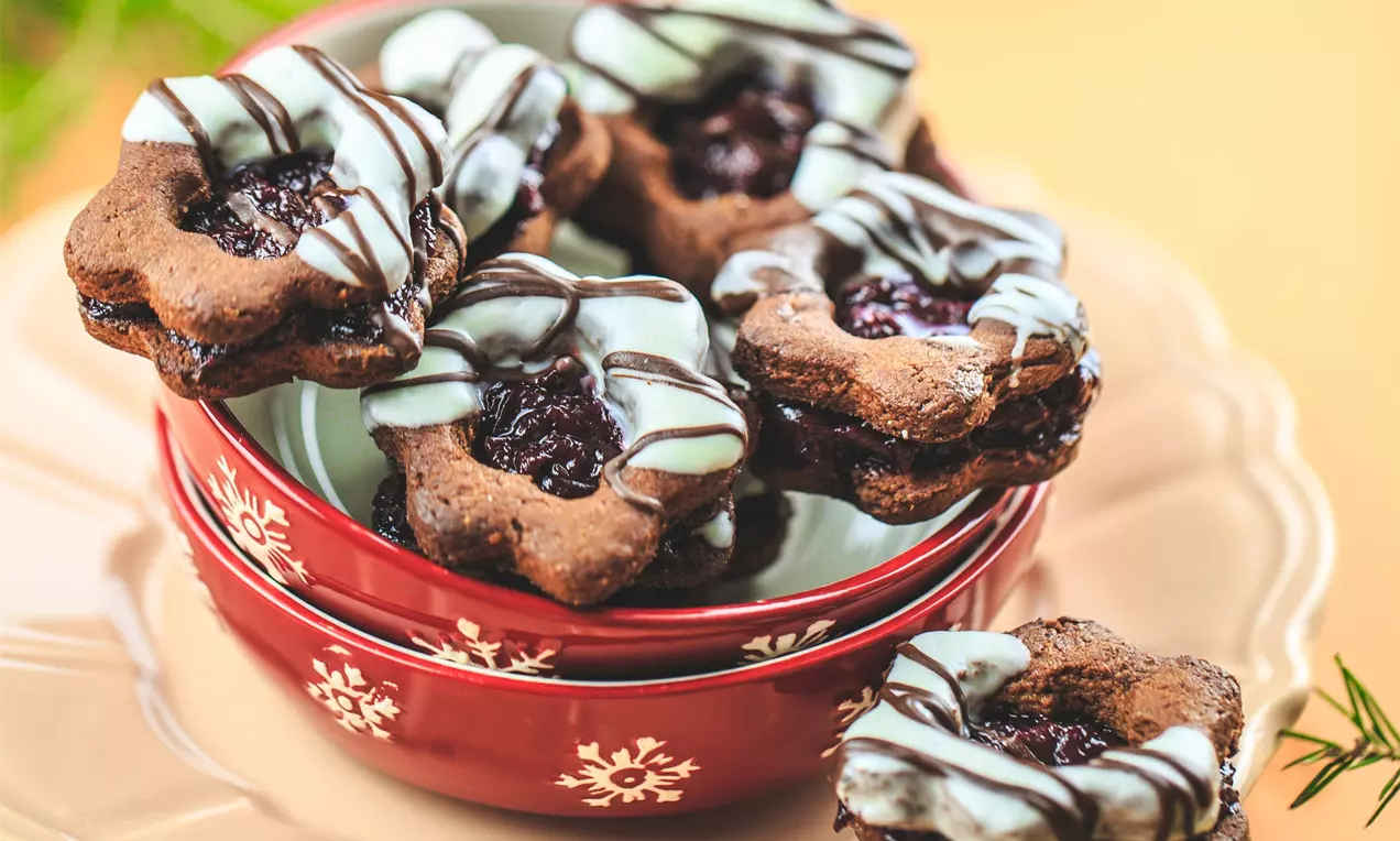 Шварцвалдски сладки с форма на цвете, кафяво тесто, пълнеж от тъмен конфитюр и бледи шоколадови ивици върху червена купа със снежинки