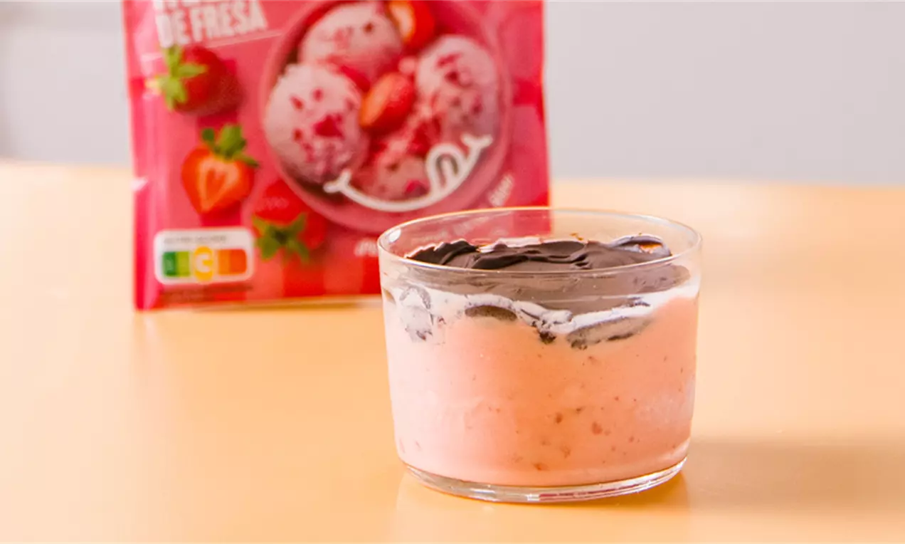 Helado cremoso de fresa color rosa suave en vaso de cristal, cubierto con una capa crujiente de chocolate oscuro