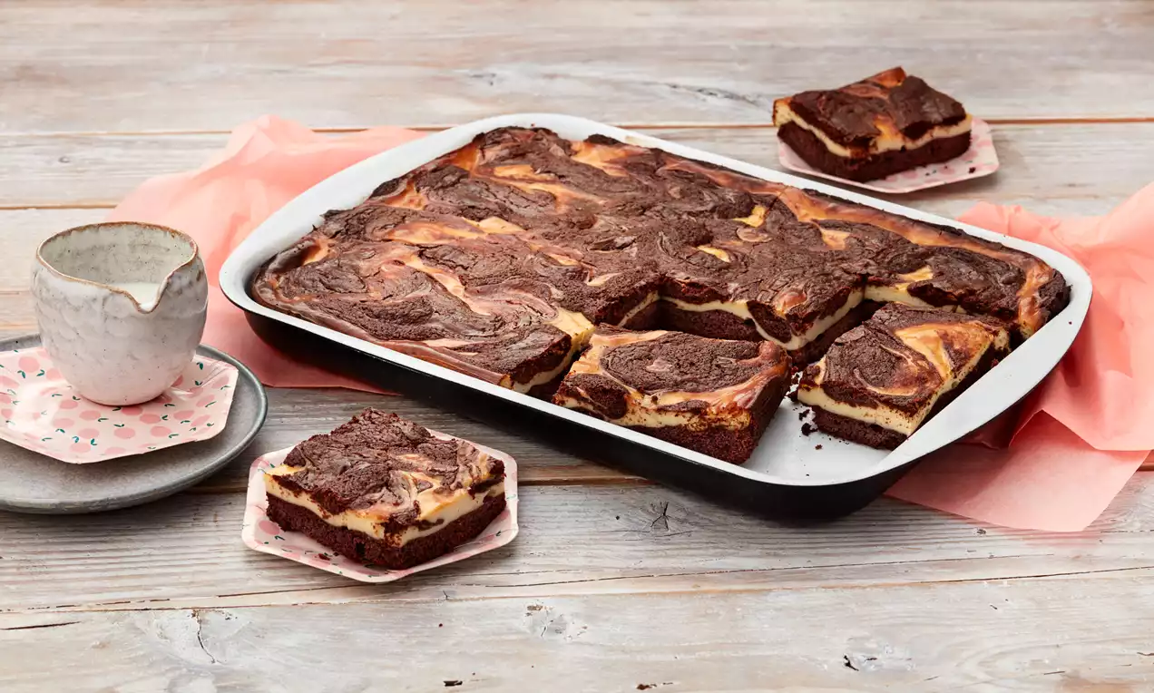Cheesecake-Brownies mit marmorierter Oberfläche aus cremigem Käsekuchen und dunkler Schokoladentextur in weißer Backform auf Holzplatte