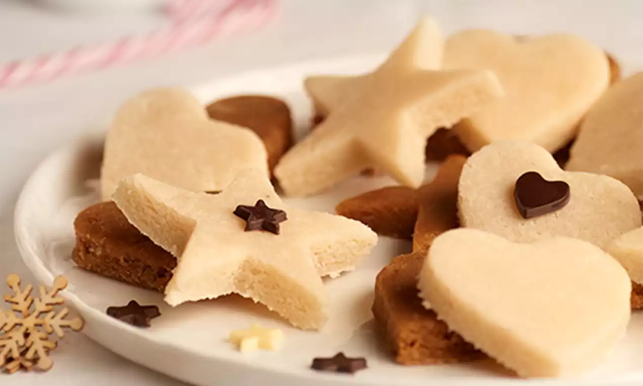 Figuras de turrón de coco beige con textura suave, moldeadas en forma de estrellas y corazones, sobre galletas marrones en un plato blanco