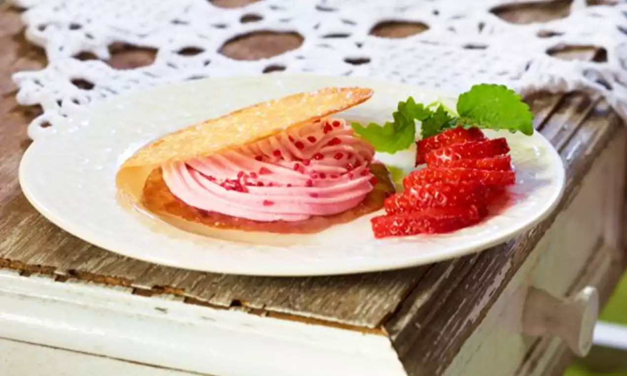 Knäckebrødformet flarn med sprø gyllen overflate, rosa kremrosetter med røde perler og friske jordbærskiver på hvit tallerken