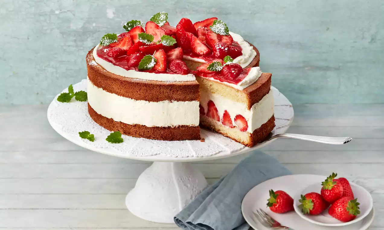 Erdbeer-Sahne-Torte mit luftigem, goldbraunem Biskuit, weißer Sahnefüllung und frischen roten Erdbeeren auf einer weißen Tortenplatte