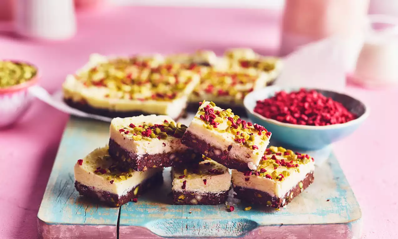 Chocolate and Milk Layer Barfi with a smooth cream top, rich brown base, pistachio and berry sprinkling on a rustic blue wooden board