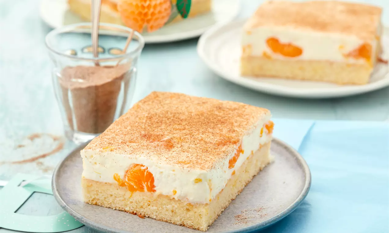 Schmandkuchen vom Blech mit cremiger weißer Schmandschicht, leuchtenden Mandarinenspalten auf goldbraunem Boden und Puderzucker