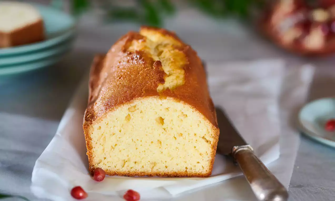 Saftig-goldbrauner Rührkuchen mit hellgelbem Teigschnitt, angerichtet auf Backpapier, daneben ein Messer und verstreute Granatapfelkerne