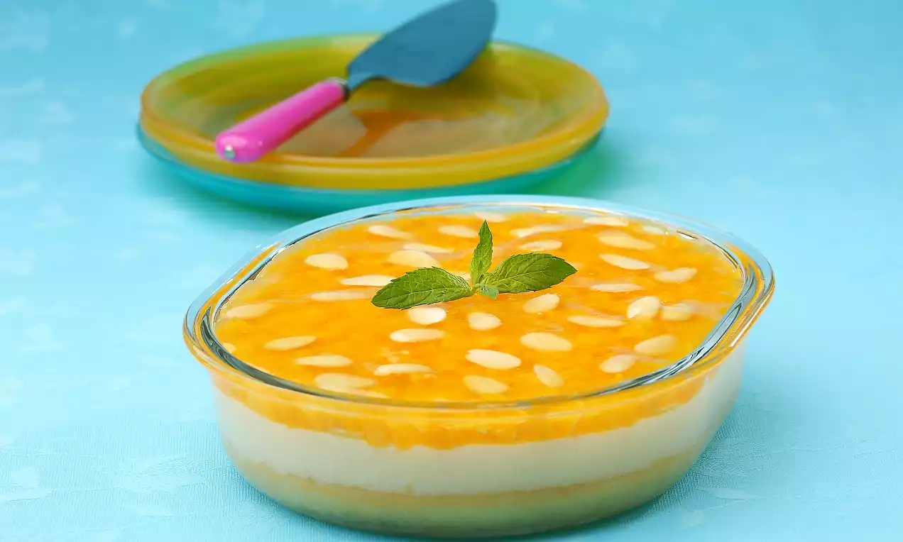 Portakal renkli akışkan sosla kaplı, badem parçaları serpiştirilmiş, şeffaf cam kapta katmanlı irmik helvası, nane dalı ile süslenmiş