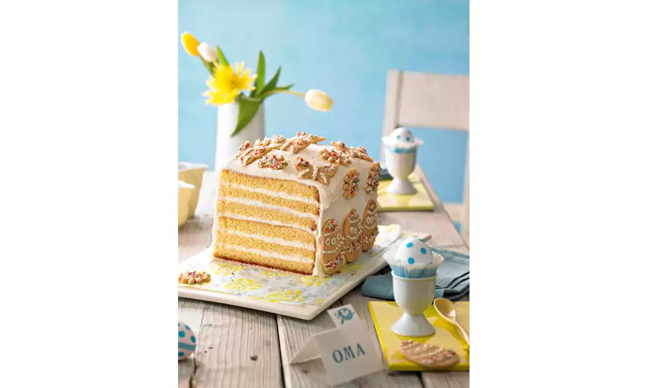 Gâteau à étages rectangulaire aux tons dorés avec glaçage blanc, décoré de formes délicates, sur une assiette blanche ornée de motifs jaunes