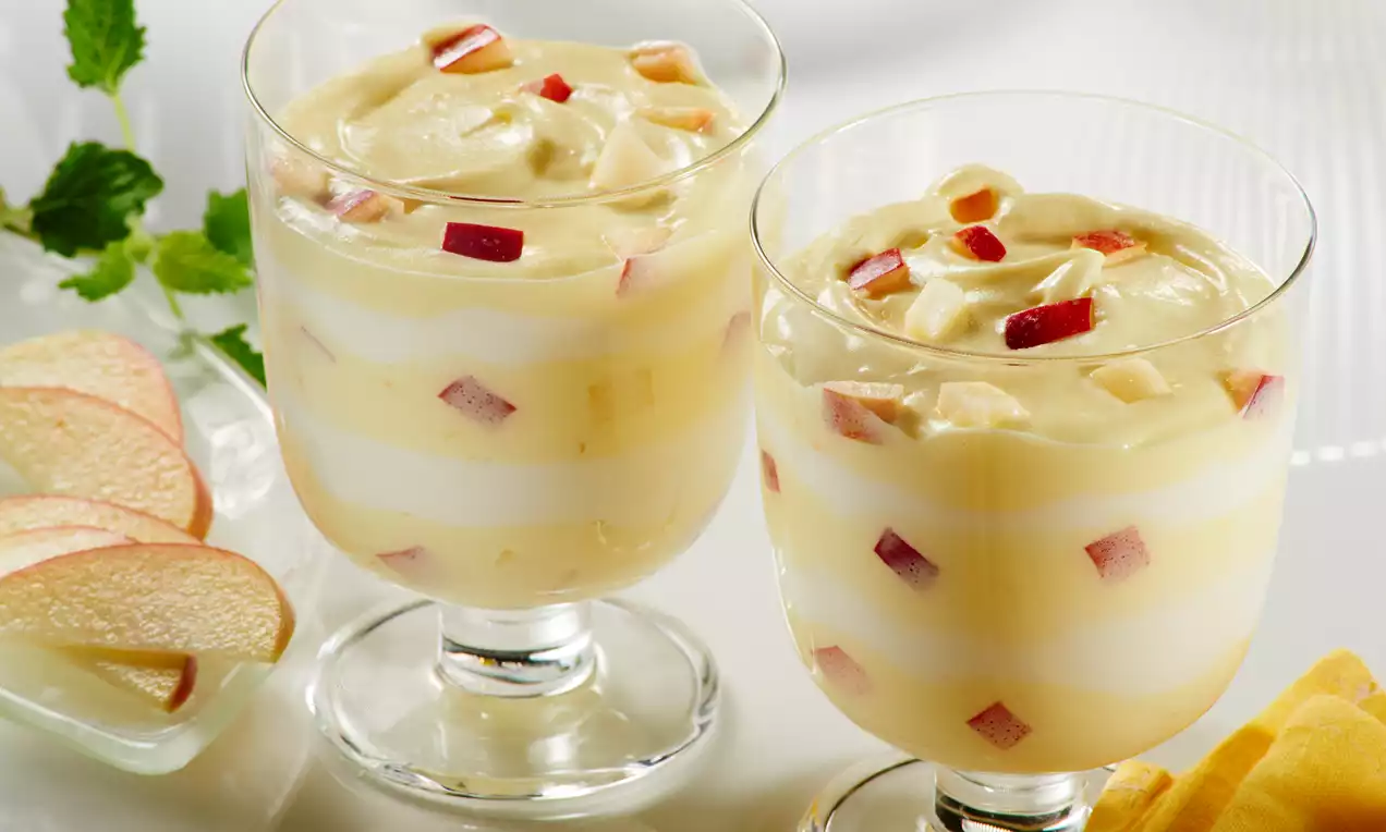 Mousse jaune pâle onctueuse en verrine avec couches marbrées, morceaux de pomme rouge et tranches de pomme en décoration