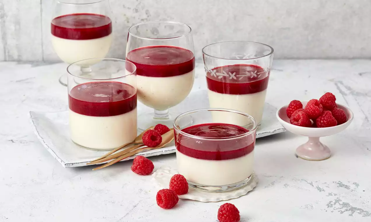 In Gläsern servierte Panna Cotta mit weißer cremiger Basis und glatter roter Himbeerschicht, dekoriert mit frischen Himbeeren auf hellem Untergrund