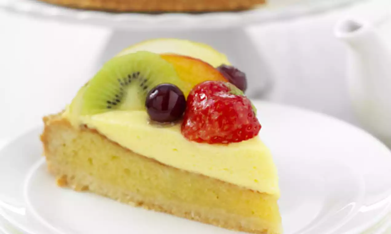 Driehoekige punt taart met een luchtige lichtgele vulling, gegarneerd met glanzend rood fruit, kiwi en perzik op een witte bordenstapel