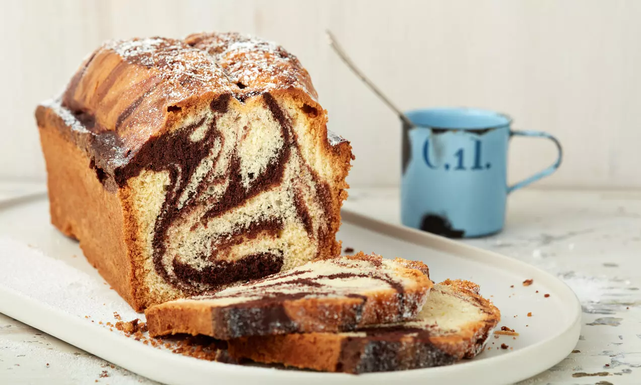 Мраморен кекс със златиста коричка и кадифени бели и черни шарки, нарязан на филии върху светла правоъгълна чиния