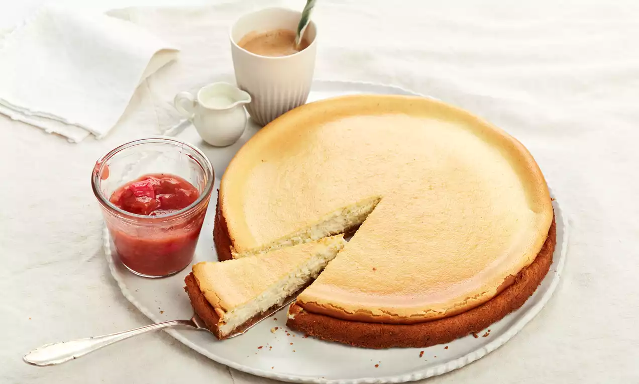 Käsekuchen mit Keksboden: goldbrauner Keksboden, cremige weiße Quarkfüllung, dünne Zitronenscheiben und Minzblatt als Garnitur