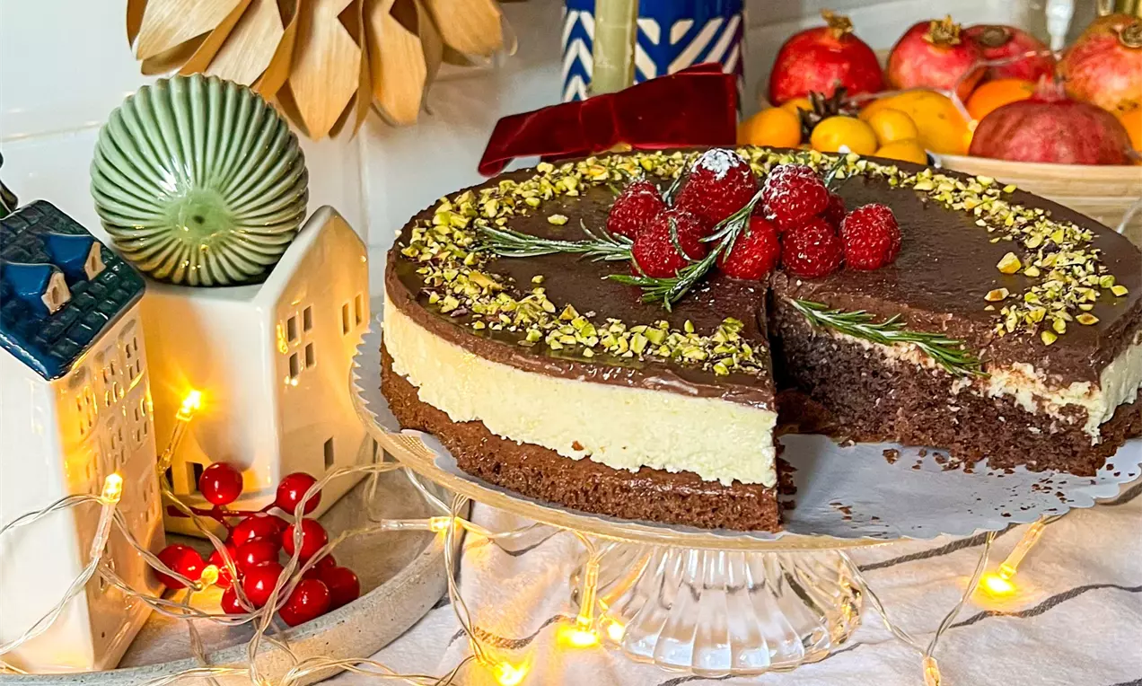 Торта с пухкав кокосов крем върху плътен шоколадов блат, покрита с гладък шоколадов ганаш, декорирана с малини, розмарин и шамфъстък