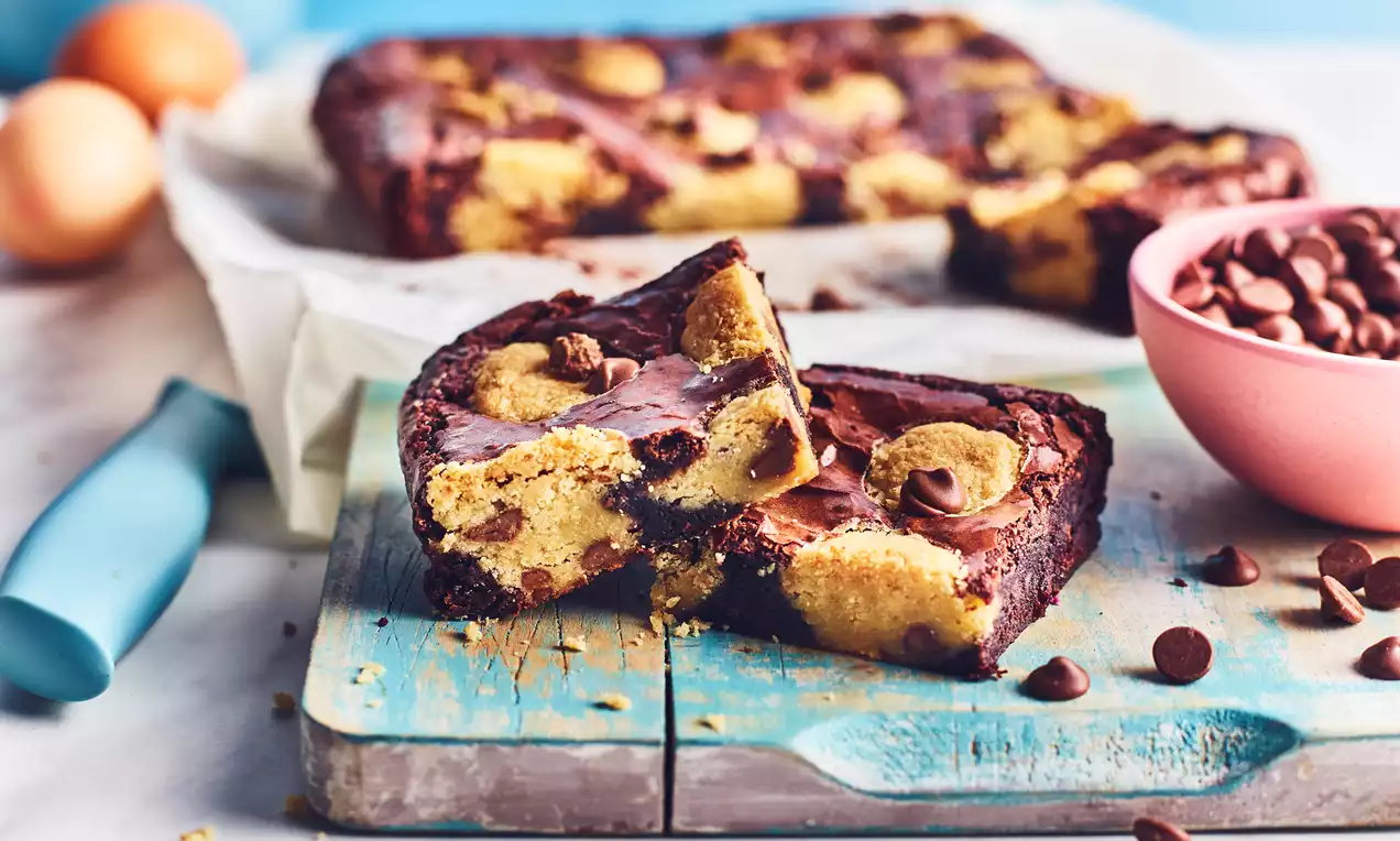 Brookies with rich golden cookie dough swirls and deep brown brownie layers, cut into squares on a rustic wooden board brushed blue