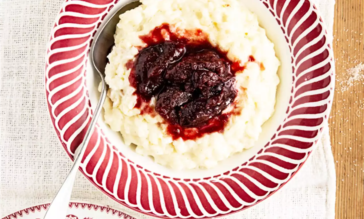 Urner Nytläriis mit cremiger weißer Konsistenz und tiefrotem Zwetschgenkompott serviert in einem rot-weiß gemusterten Teller auf weißem Stoff
