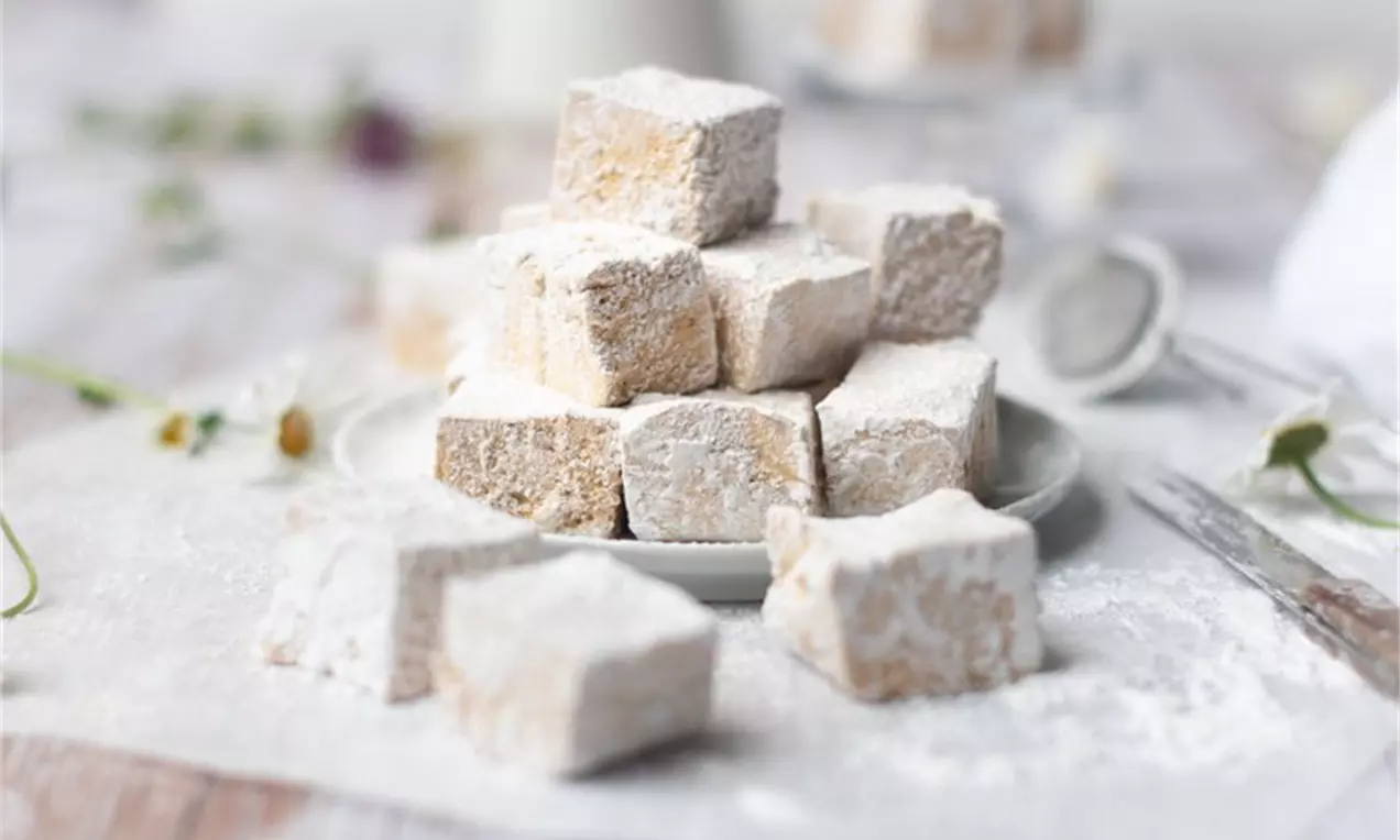 Selbstgemachte Marshmallows in Würfelform, weich und luftig mit weißem Puderzucker bestäubt und auf einem Teller kunstvoll gestapelt